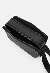 Black leather crossbody bag with two zippered compartments, textured finish, detachable strap, and silver hardware accents.