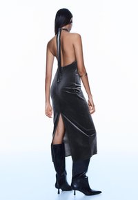 Tmavomodré hodvábne šaty s halterovým výstrihom, bez chrbta, so zákrokom na boku, nosené s čiernymi čižmami po kolená.