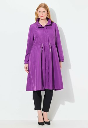 Purple, lightweight, long coat with a cinched waist, button front, and high collar; paired with black leggings and heels.
