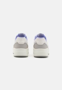 Białe i jasnoszare trampki z teksturowanym obcasem i lawendowymi akcentami. Zaokrąglony design z siateczkowymi detalami na kołnierzu i języku.