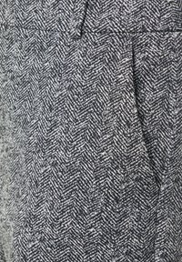 Schwarzes und weißes Hahnentrittmuster mit einer ausgeprägten Struktur und leichtem Glanz, das im Bereich der Taille eine Faltenoptik aufweist.