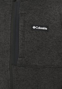 Veste en polaire gris foncé texturée avec une fermeture éclair noire et un petit patch noir affichant le logo Columbia blanc sur la poitrine.