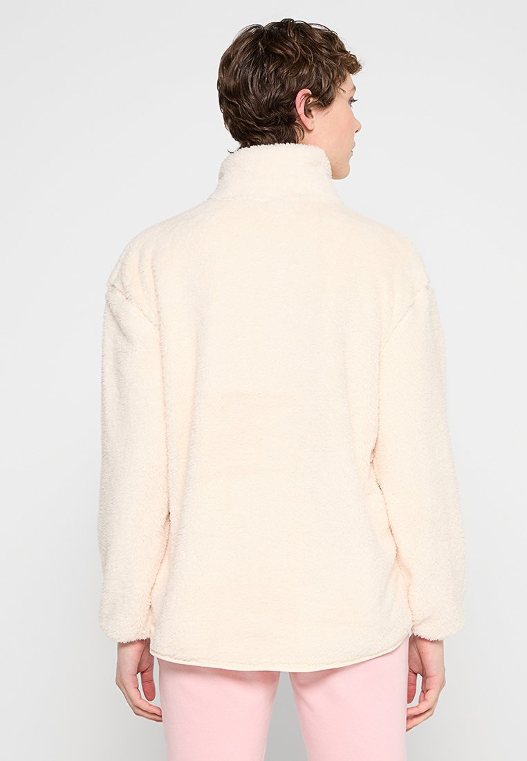 Pull en polaire beige clair, col haut, manches longues, coupe décontractée, texture douce, design uni, coutures latérales et ourlet incurvé à la taille.