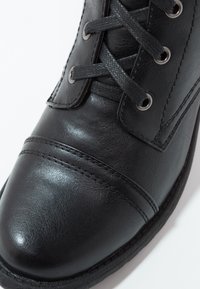 Botín negro de cuero hasta el tobillo con punta redonda, frente texturizado, costuras reforzadas y ojales plateados para los cordones. Acabado suave con acentos mate.