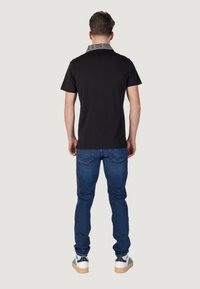 Polo negro con cuello gris, combinado con jeans de mezclilla azules y zapatillas blancas con detalles en negro y verde.