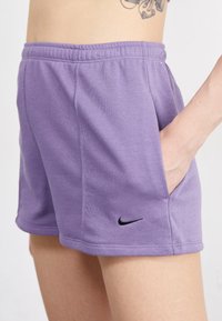 Pantaloni corti viola di cotone con cintura elastica, tasche laterali e logo Nike nero sulla parte inferiore dell'orlo. Tessuto liscio e vestibilità casual.