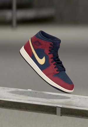 Baskets montantes rouges et bleu marine avec un swoosh Nike beige flottant au-dessus d’un banc en béton dans un environnement intérieur neutre.