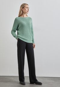 Světle zelený pletený svetr s volným střihem a žebrovanými manžetami, zkombinovaný s volnými černými kalhotami a masivními černými botami.