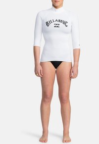 Vitt långärmad rash guard med svart "BILLABONG"-logotyp. Designad för vattensporter, med en åtsittande siluett och stretchigt material.