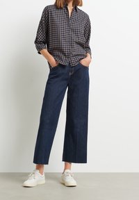 Chemise à boutons à carreaux bleu marine en coton, associée à un jean denim foncé à jambes larges et des baskets blanches. Dispose de poches avant et d'ourlets effilochés.