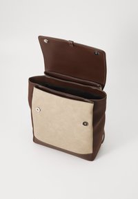 Sac en cuir marron et beige avec un rabat, ferrures argentées et deux compartiments intérieurs. Texture lisse et détails de couture contrastés.