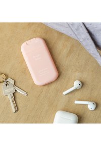 Botella de desinfectante de manos rosa etiquetada "Rosa Brillante" junto a unos auriculares inalámbricos blancos y llaves sobre una superficie de madera.