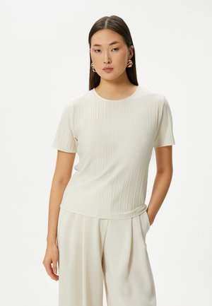 Lys beige kortærmet top med lodret ribbet tekstur, rund hals og slim fit, båret med cremede, vide bukser.