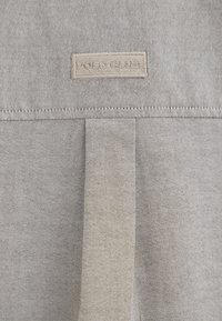 Tessuto grigio con una trama testurizzata. Presenta un'etichetta cucita con la scritta "POLO CLUB" in beige. Due pieghe sono visibili nel design del tessuto.