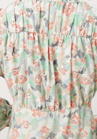 Blommönstrad klänning i mjukt tyg; pastellfärger inklusive rosa, grön och svart; sammanknuten midja och puffärmar. Texturerad yta.