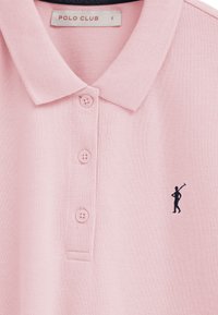 Polo rose clair avec col, trois boutons assortis et une petite figure noire brodée sur la poitrine, étiqueté "Polo Club" taille S.