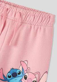 Pantaloni felpati rosa chiaro con vita elasticizzata, caratterizzati da una stampa grafica di due personaggi dei cartoni in blu e rosa. Texture in cotone liscia.