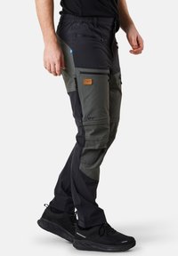 Pantalons cargo avec panneaux noirs et verts foncés, plusieurs poches zippées, taille élastique et sections de genoux renforcées.