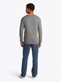 Sweater cinza de manga longa com decote redondo, punhos canelados e um corte relaxado, combinado com calças azuis e sapatilhas brancas.
