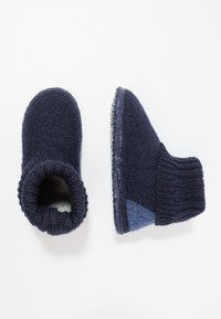 Marine blauwe vilten pantoffels met een gebreide boord, ronde neus en een rubberen zool. Een zijaccent heeft een lichter blauw stoffen patch.