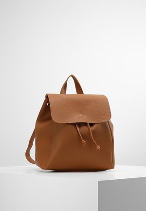 Bruine rugzak van getextureerd leer met klep- en trekkoordsluiting, voorzien van een handvat bovenaan en verstelbare schouderbanden, tentoongesteld op een wit voetstuk.