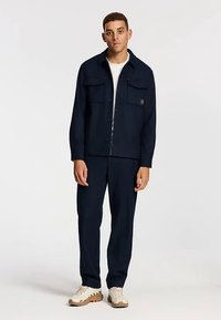 Mornarsko plava jakna s dva džepa na prsima, gumbima sprijeda i odgovarajućim hlačama. Glatki materijal s opuštenim krojem, uparena s laganim tenisicama.