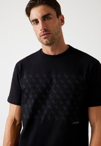 Zwarte katoenen t-shirt met een diamanten patroon en logodetail in een donkerdere schaduw. Klassieke ronde hals en korte mouwen.