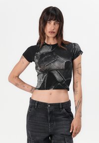 Black cropped t-shirt featuring a printed design resembling denim with varying textures. Short sleeves and a round neck. Skin is visible below the hem.