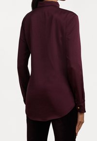 Langärmlige burgunderfarbene Bluse aus glattem Material mit Kragen und geknöpften Manschetten. Verfügt über einen abgerundeten Saum und dezente Steppdetails.