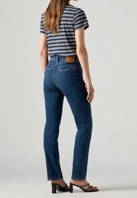 Jean en denim bleu à taille haute et jambe droite, avec une patch en cuir à l'arrière et des coutures contrastées. Haut à manches courtes à rayures.