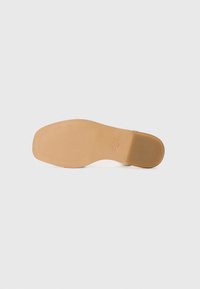 Semelle de chaussure beige avec une finition lisse, motif nervuré pour une adhérence, et une légère courbure au niveau du talon. Marque présente sur le côté.