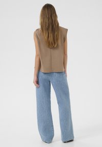 Un top fără mâneci de culoare maro, relaxat, cu un tiv rotund, asociat cu pantaloni largi de culoare albastru deschis, cu un model texturat.