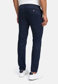Marineblå chinos med slim fit, der har to baglommer med knapper og en læderlogo mærke. Glat stoftekstur, parret med hvide sneakers.