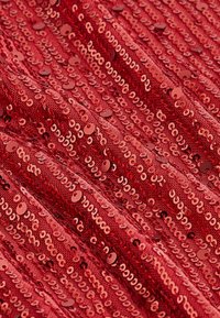 Tissu rouge densément recouvert de paillettes brillantes disposées en rangées diagonales, créant une surface texturée et réfléchissante.