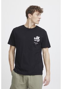 Sort bomulds T-shirt med et hvidt blomstermotiv på venstre bryst. Regular fit med rund hals. Minimalistisk design, glat tekstur.