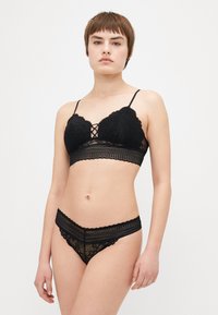 Svart blond lingerie-set som inkluderer en bralette med bølgete kanter, blonderdetaljer og justerbare stropper, kombinert med matchende blonde truser.