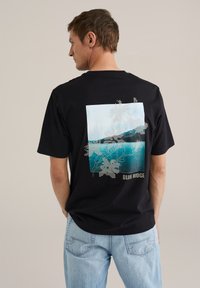 Fekete pamut póló, hátoldalán grafikus nyomattal, amelyen egy kék tó jelenet és virágos körvonalak láthatók, az alján "BLUE RIDGE" felirattal.