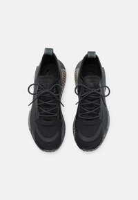 Svarta sportskor med överdel i nät, texturerade detaljer och snören. Har en mönstrad mellansula och en dragflik på hälen för enkel påtagning.