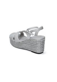 Vita wedge-sandaler har korsade remmar och en strukturerad silverplattform med ett vävt mönster. Sulan är av svart gummi för bra grepp.
