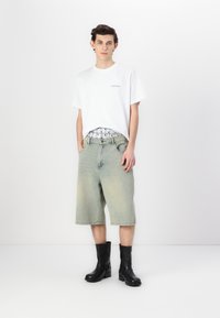Hvit bomull t-skjorte med minimal tekst, lyseblå denimshorts, svarte ankelstøvler. Shortsene har lommer, avslappet passform og falmet farge.