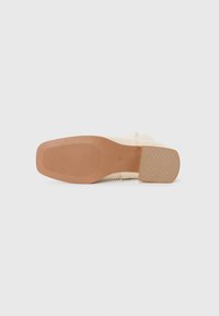 Semelle de chaussure beige avec une surface en caoutchouc texturée, un talon rectangulaire et un motif strié pour une meilleure adhérence. Matériau doux sur les côtés.