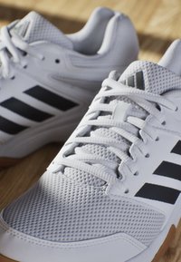 Baskets blanches de sport avec une tige en maille texturée, un design à trois bandes noires et des accents gris. Comprend une languette rembourrée et une semelle en caoutchouc.