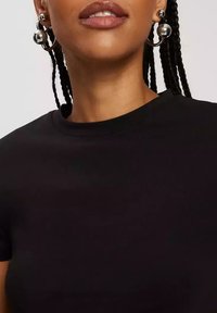 Czarna krótka koszulka z okrągłym dekoltem, wykonana z gładkiego materiału i dopasowana. Srebrne kolczyki w formie obręczy z kulkami dodają detalu.