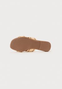 Beige kile sandal med vevde stropper og en glatt brun såle. Har en rund tå og flat bunn for stabilitet.