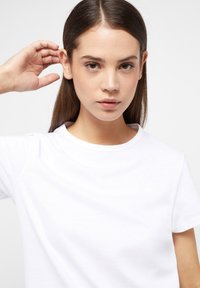 Bílá tričko s krátkým rukávem a kulatým výstřihem, vyrobené z hladké bavlněné tkaniny. Obsahuje minimalistický design bez viditelných vzorů nebo dekorací.