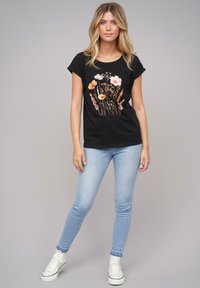 Svart bomull t-skjorte med blomster grafisk design i pastellfarger, kombinert med lyseblå skinny jeans og hvite høye sneakers.