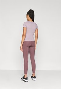 Camiseta lilas ajustada de manga corta, combinada con leggings en tonos malva de cintura alta y texturizados, y zapatillas deportivas negras. Tela suave y elástica.