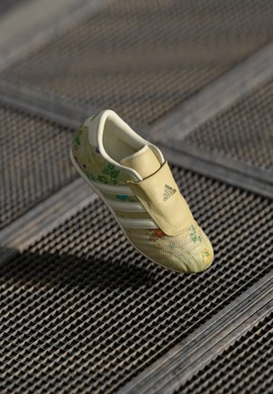 Šviesiai geltonos sportinės bateliai su gėlių raštais ir baltais akcentais, su lengvai užsimovimu ir tekstūruota paviršiumi, užtikrinančiu sukibimą.