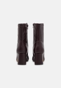 Bottes cavalières en cuir marron avec un talon carré, dotées de fermetures éclair latérales et d'un détail de couture à l'arrière pour un intérêt visuel accru.