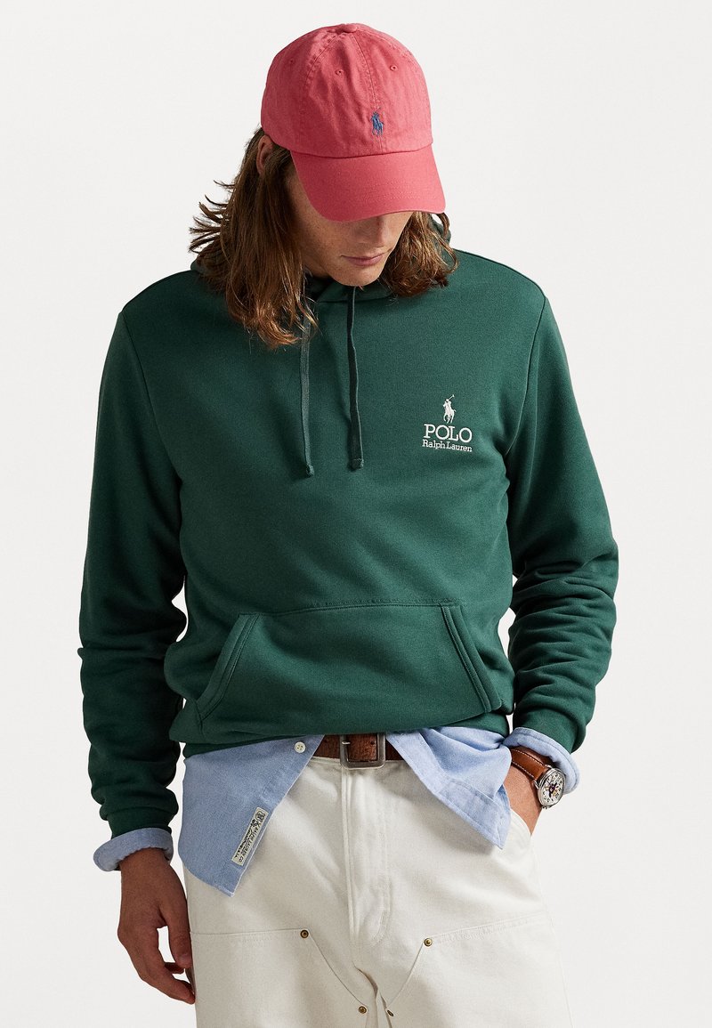 Zelená bavlnená mikina s klokankou a kapucňou na sťahovanie, s bielym logom "Polo Ralph Lauren". Nosená cez svetlomodrú košeľu na gombíky.